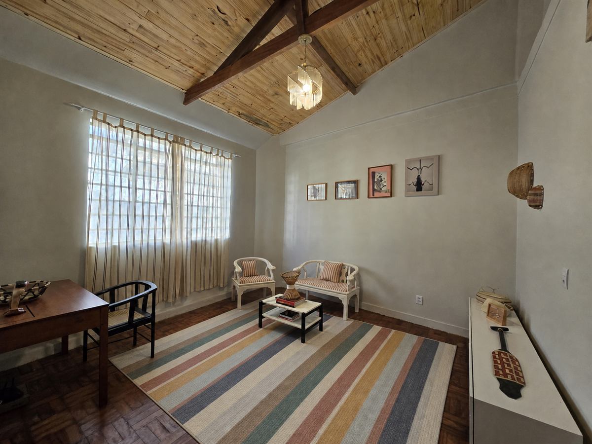 Sala da Casa Tempo Coreto com teto de bambu, tapete listrado, poltronas e janelas com cortinas claras