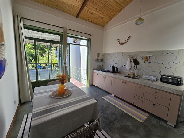 Cozinha do Apartamento 1 com armários rosados, mesa de jantar e porta de vidro para o verde