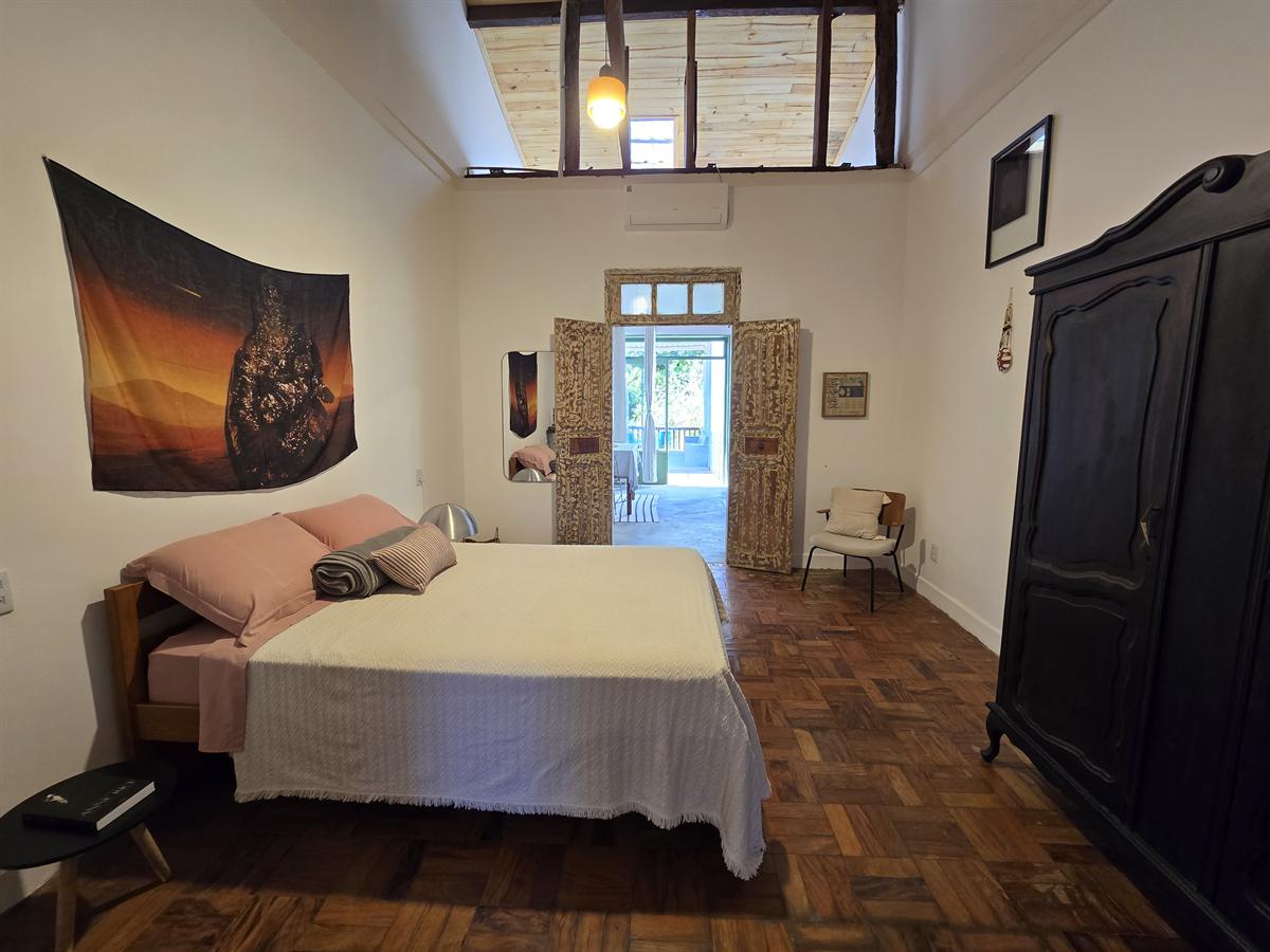 Quarto do Apartamento 1 com cama de casal, armário escuro antigo, tapeçaria na parede e portas abertas para a varanda