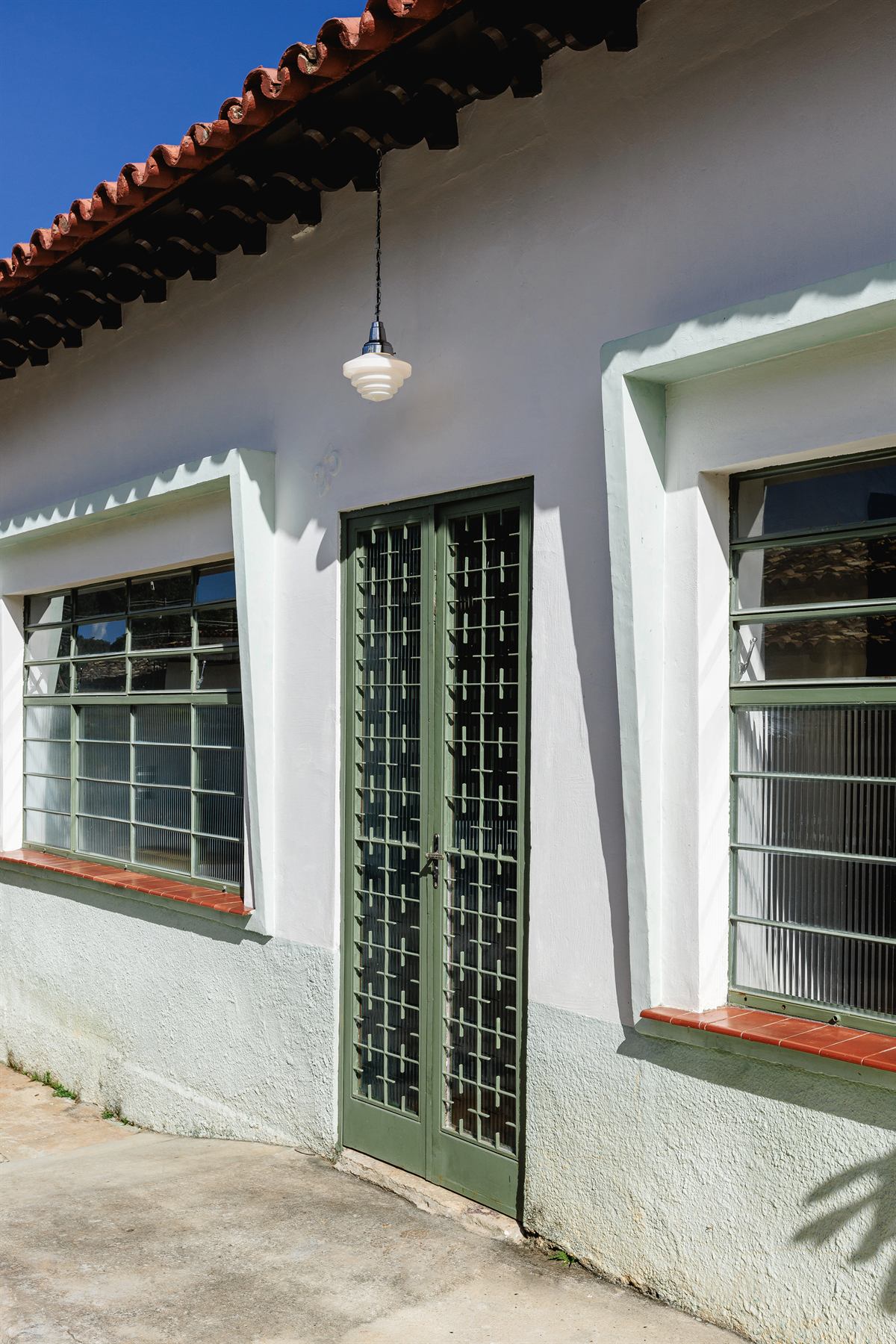 Fachada colonial branca com janelas de grade verde e beiral de telhas, vista da calçada