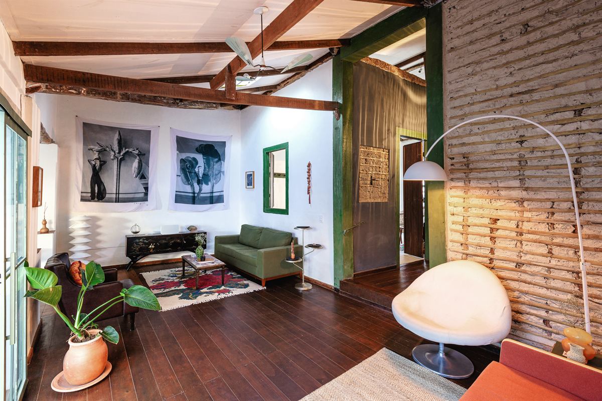 Sala com poltrona branca, luminária de arco, sofá verde e fotografias em preto e branco na parede