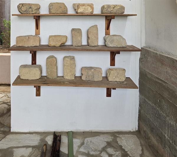 Prateleiras de madeira com pedras e fragmentos antigos expostos numa parede branca