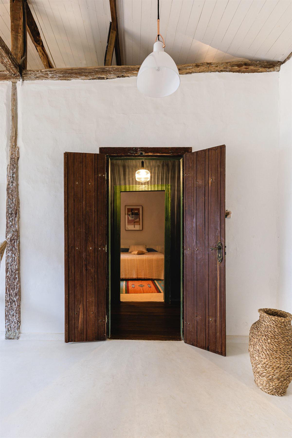 Portas de madeira de época abertas entre paredes caiadas, com vaso de cerâmica no chão