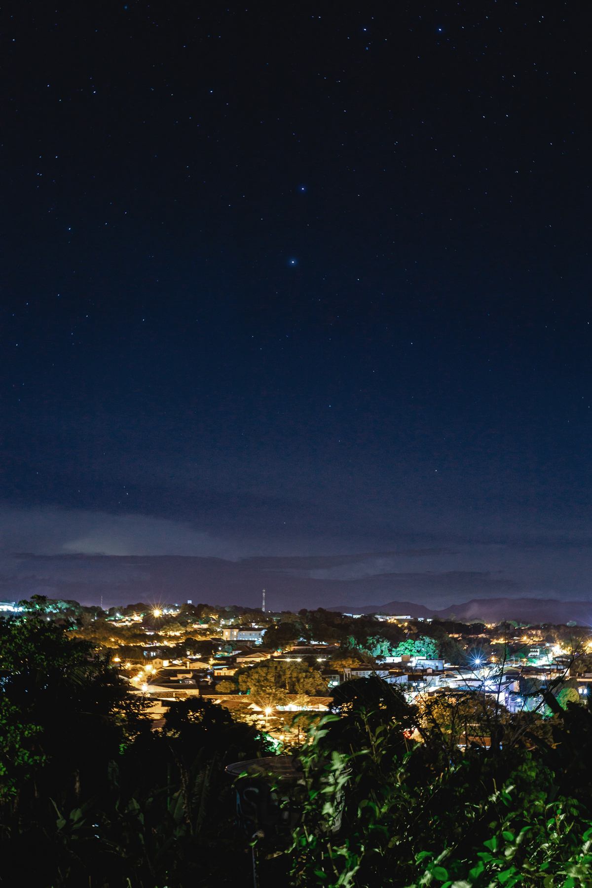 Luzes da Cidade de Goiás vistas à noite do alto da mata, sob céu azul-escuro